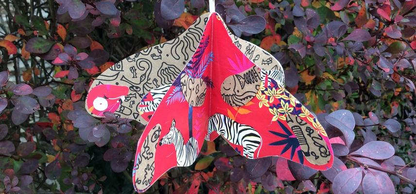 Paper moth decoration hanging in front of purple-leaved bush